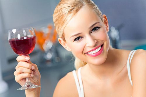 woman smiling holding a wine glass filled with red wine