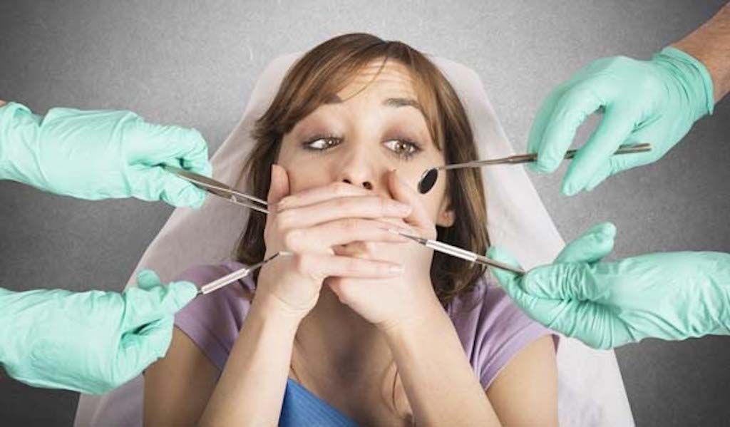woman in dentist chair covering her mouth in fear