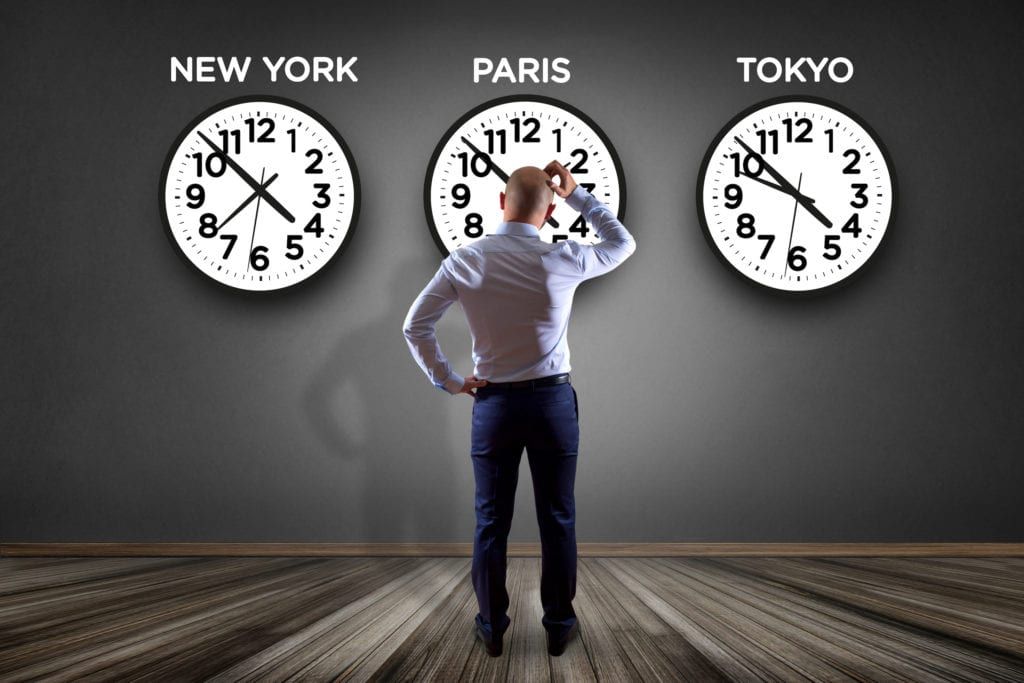 man standing in front of clocks from different time zones