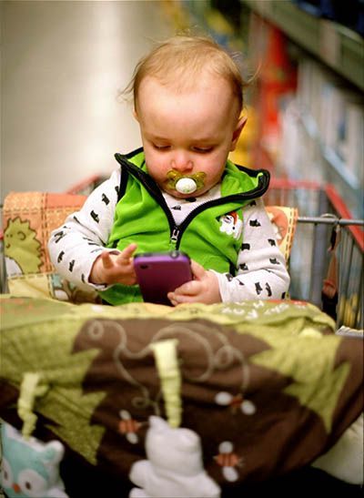 toddler in shopping cart playing on a cell phone