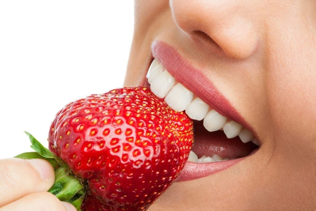 closeup of a woman biting into a strawberry