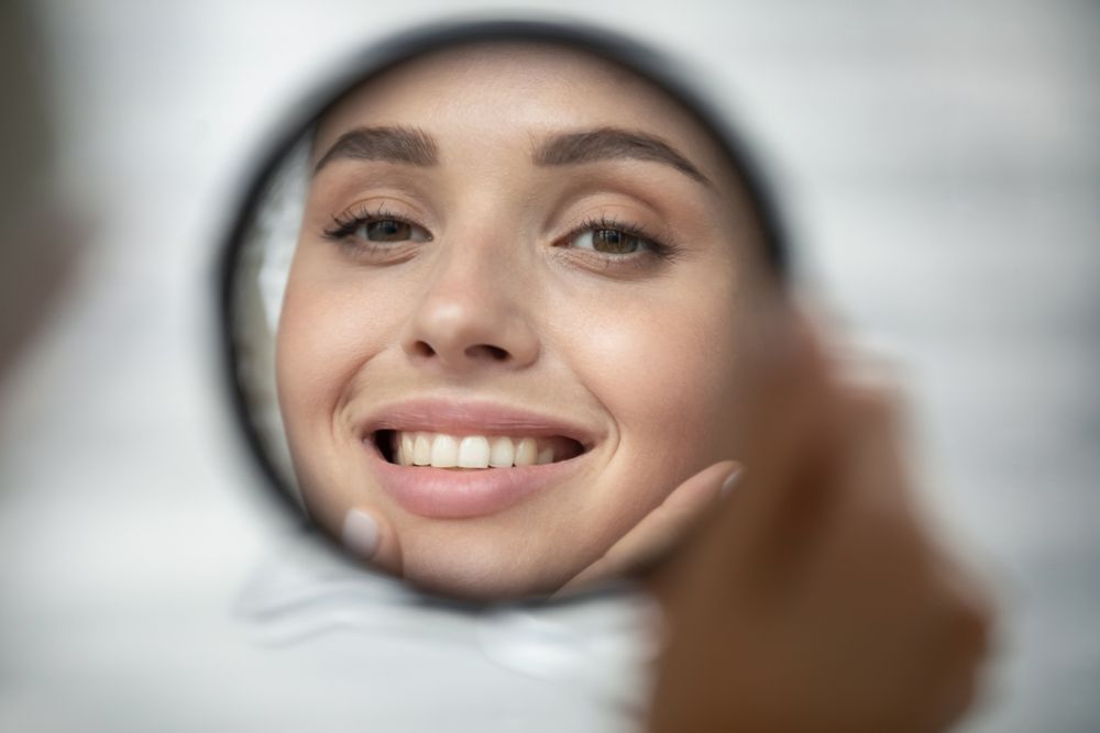 A woman looking at her smile in a hand mirror after a Smile Brightening treatment